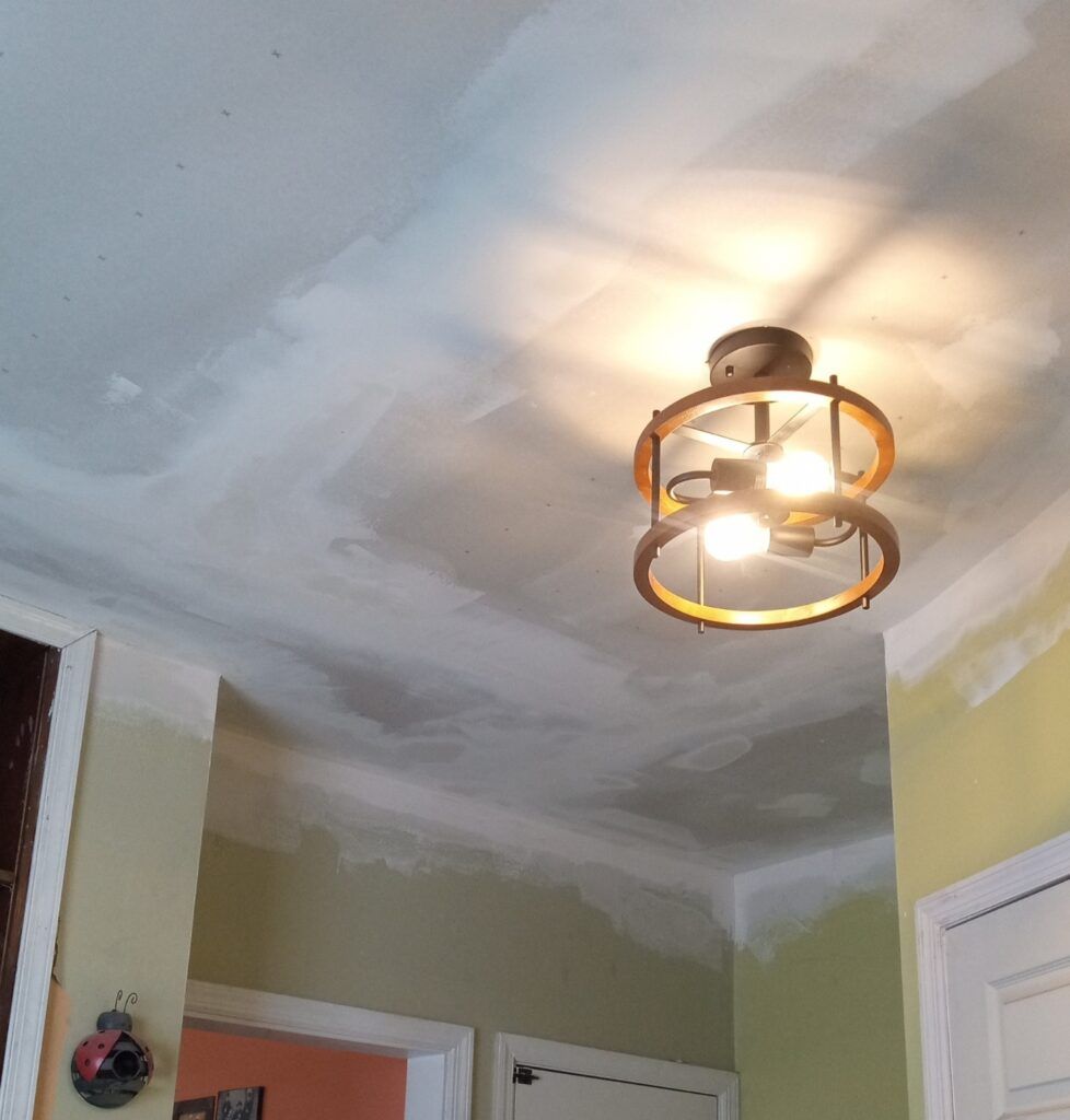 Ceiling with a light fixture. Yellow and white walls, with visible patch work.