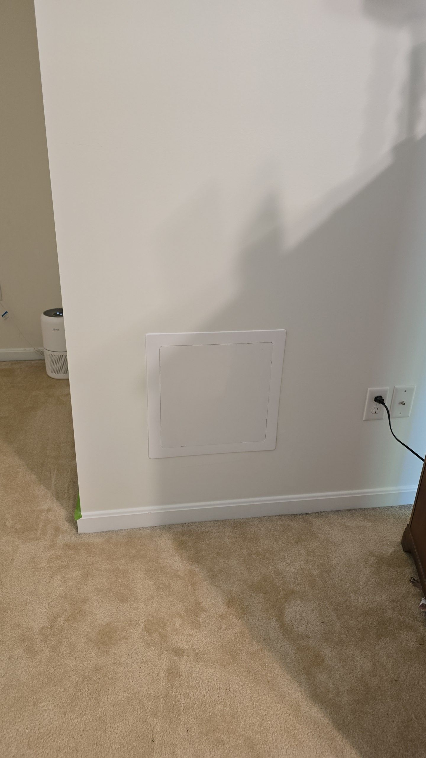 White access panel on a wall, near a floor with beige carpet and a power outlet.