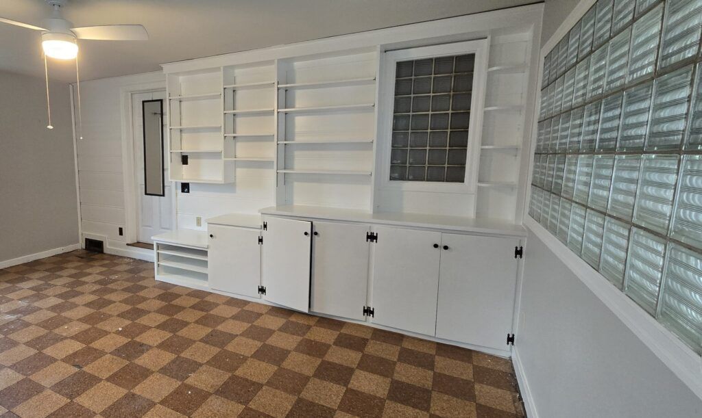 Room with built-in white shelves and cabinets. Checkered floor and a glass block wall.