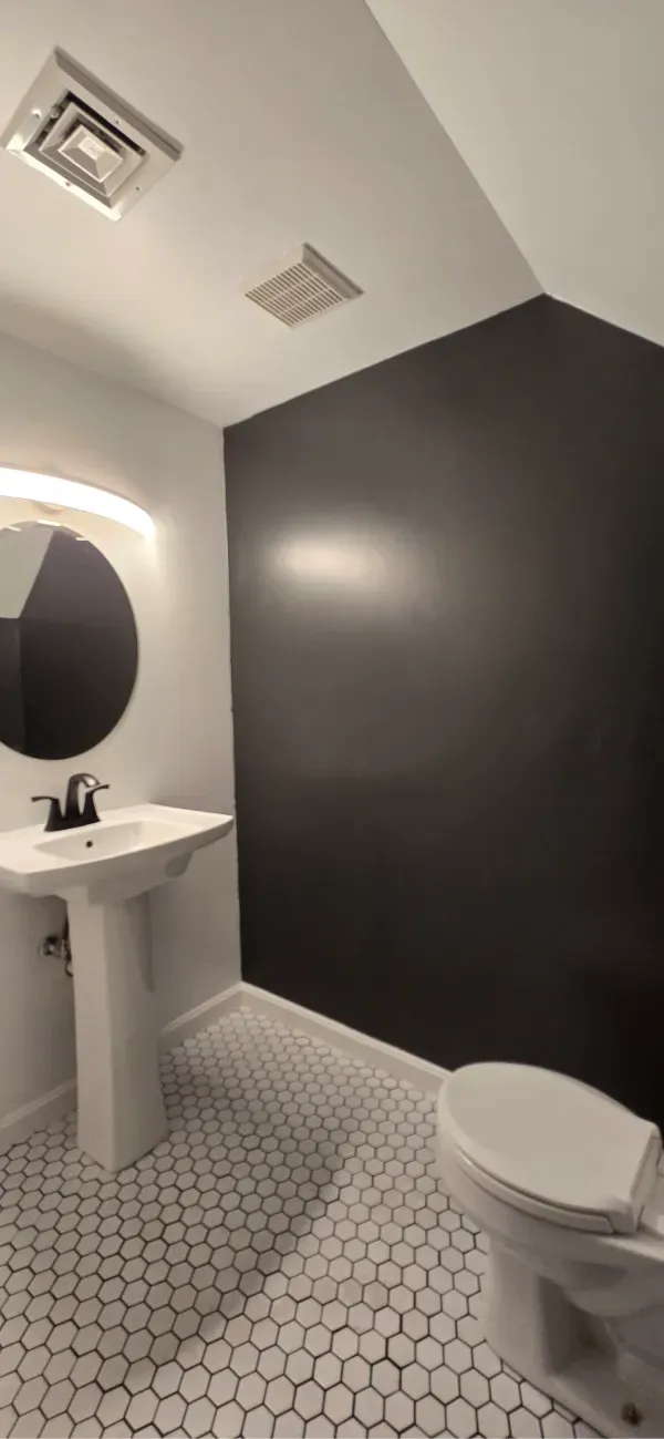 Bathroom with black accent wall, white pedestal sink, and hexagonal tile floor.