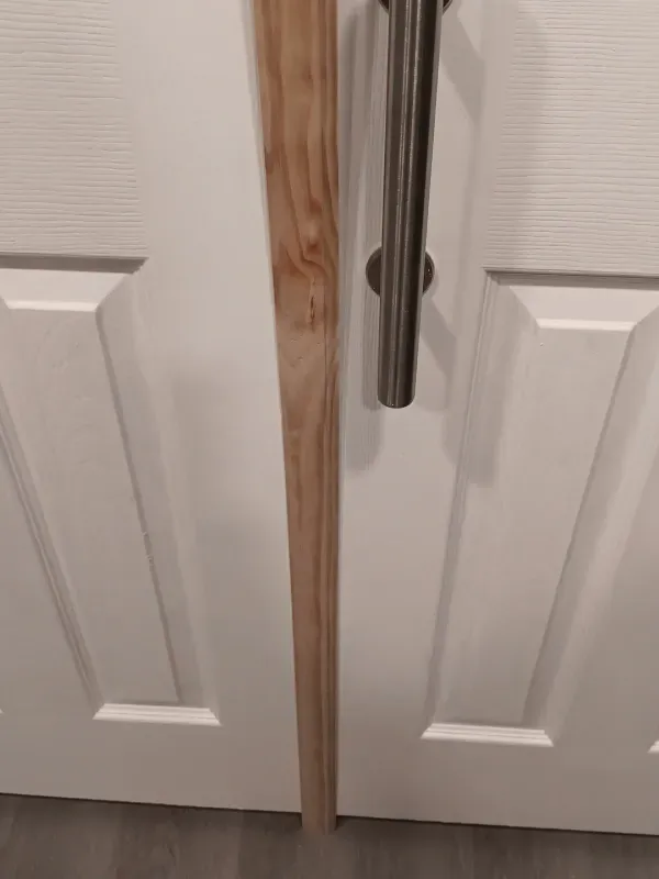 Wooden cane next to a white door with a silver handle.