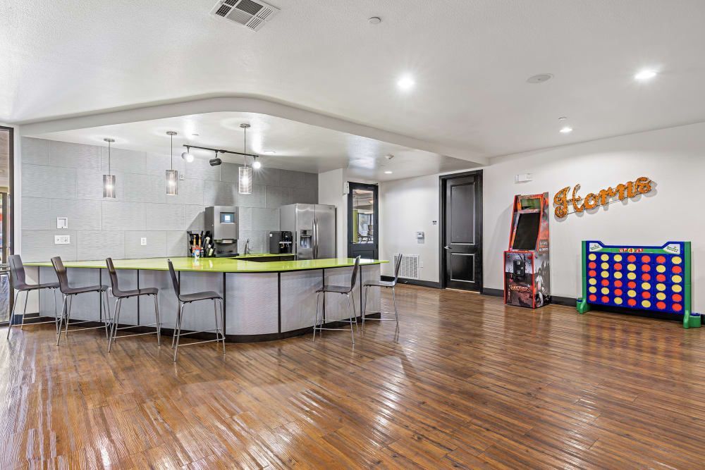 Apartment clubhouse with a wooden floor, a bar island, chairs, and games at Regents West at 24th in Austin, TX, near West Campus.