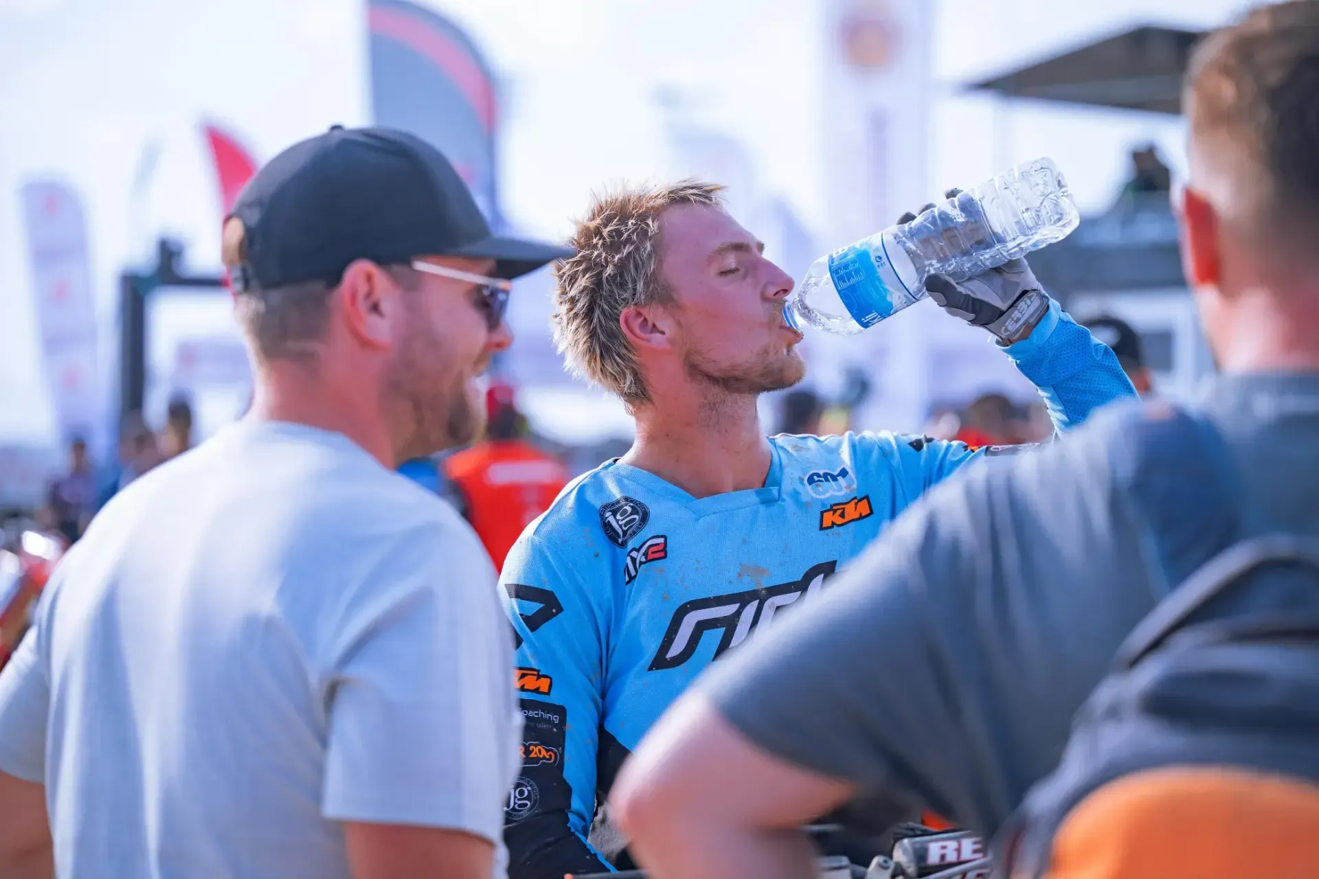 A man is drinking water from a bottle while standing next to two other men.