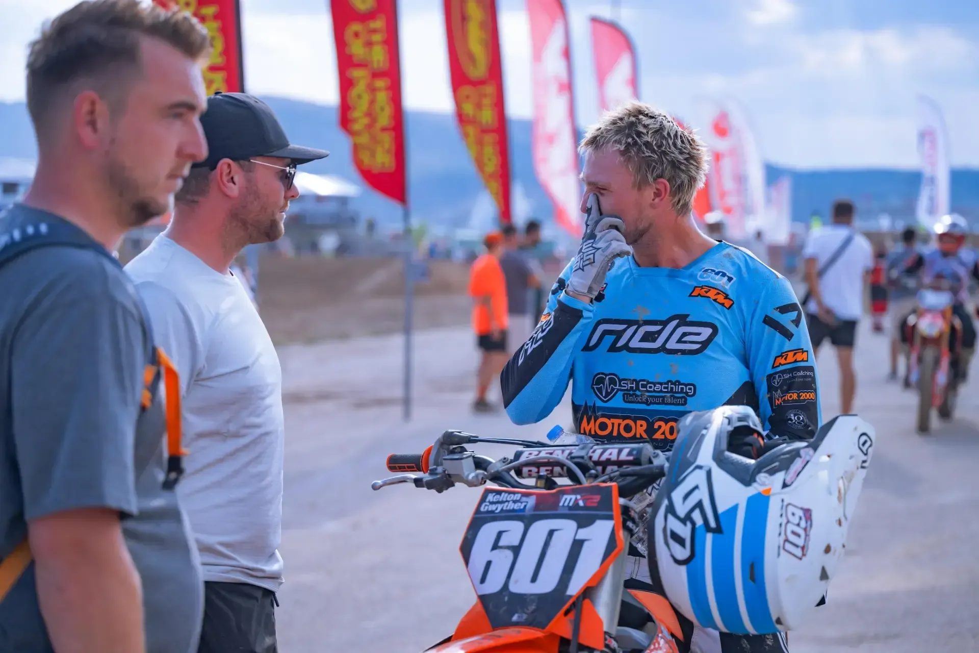 A man is talking to another man while standing next to a dirt bike.