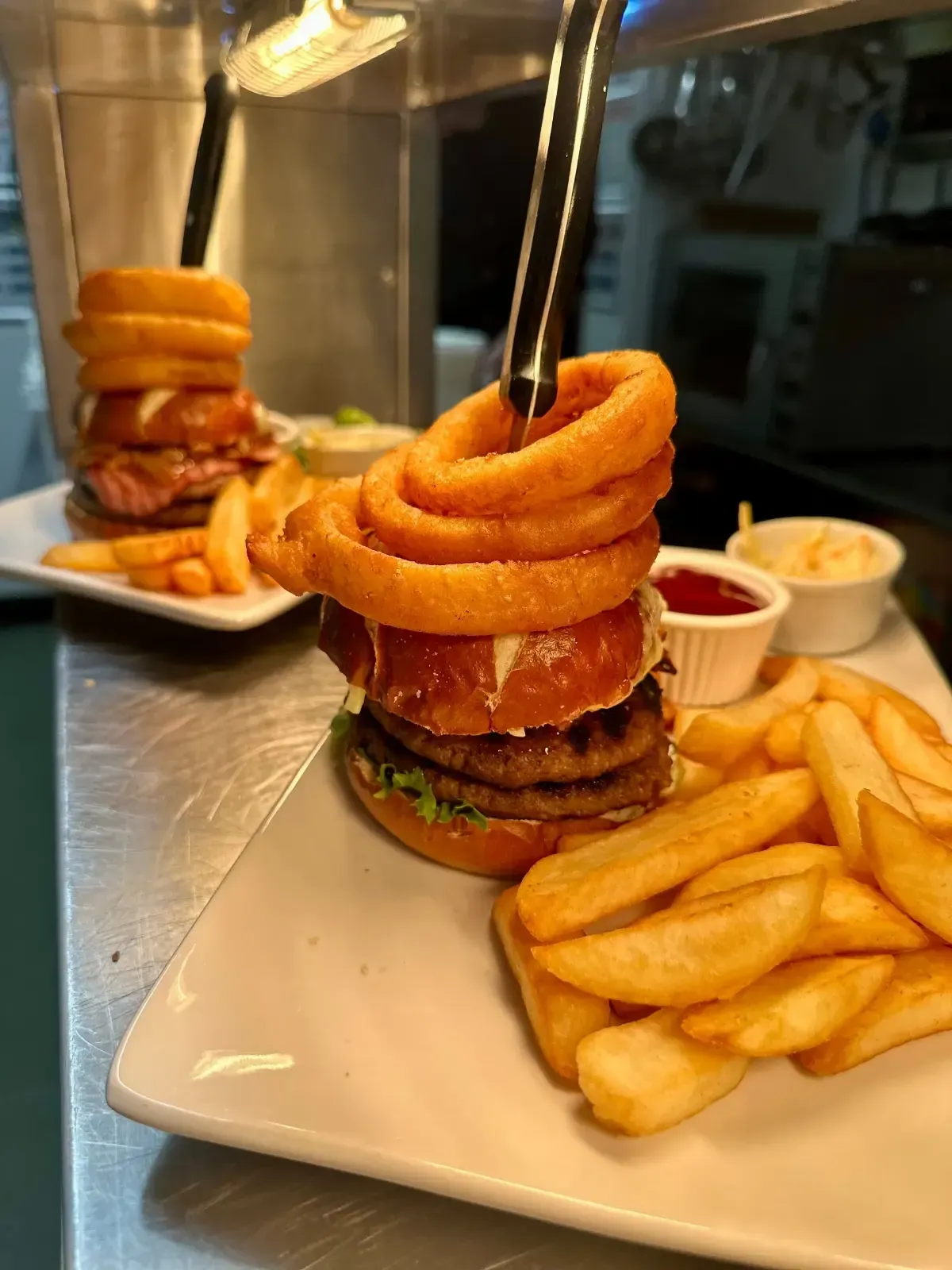 Mackworth Arms, Kids Menu | Two stacked burgers with onion rings, fries, and condiments on a white plate.