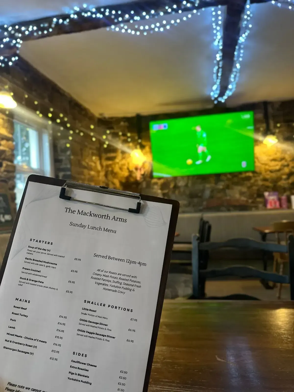 The Mackworth Arms, Laleston, Bridgend | Menu on clipboard in pub, TV on wall, string lights.