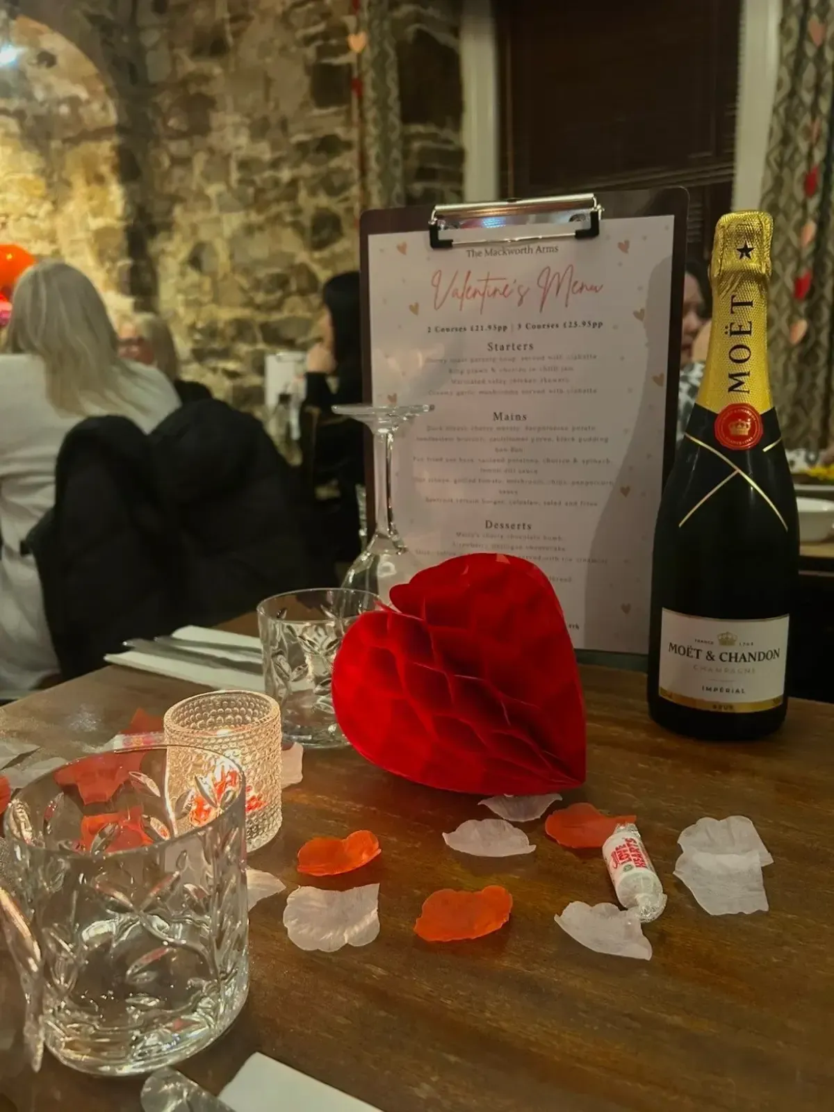 The Mackworth Arms, Laleston, Bridgend | Valentine's Day table setting with champagne, menu, heart decor, and rose petals.