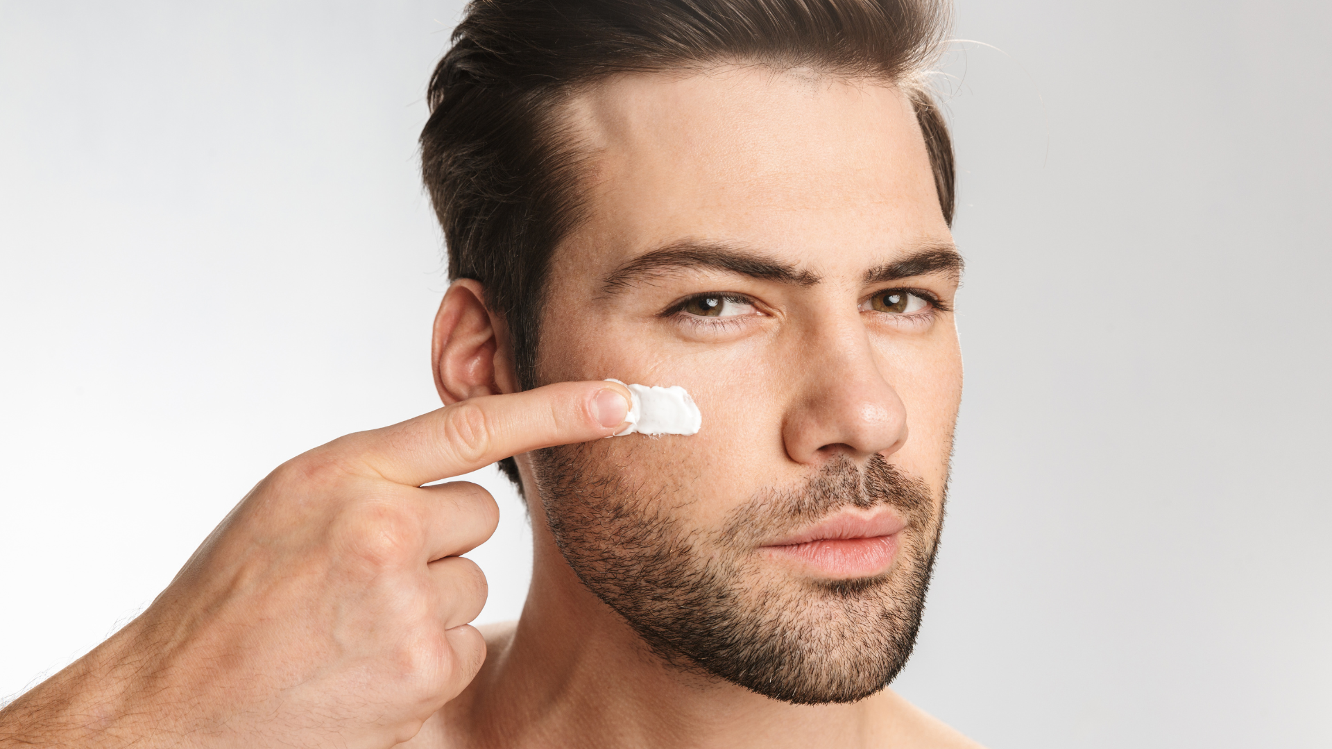 A man with a beard is applying cream to his face.