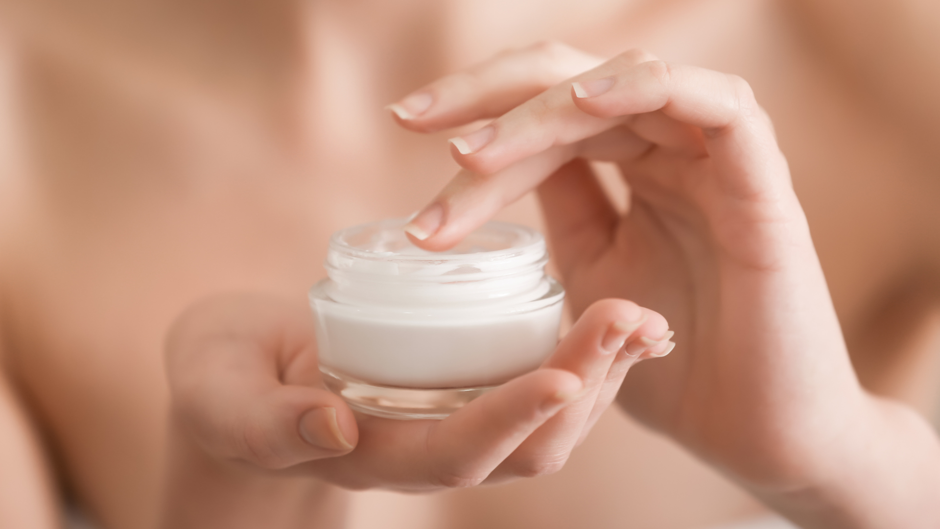 A woman is applying cream to her face from a jar.