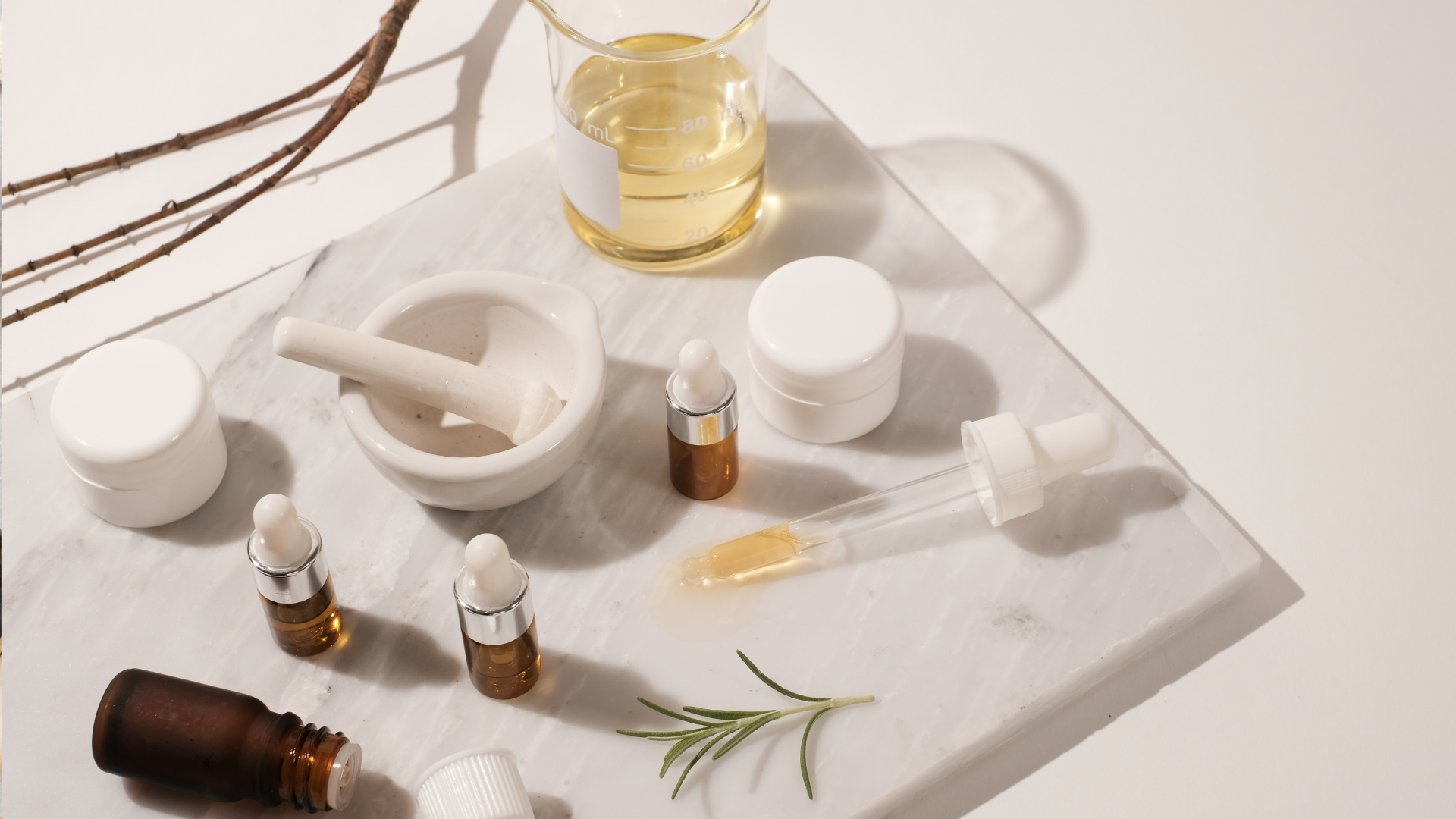 A marble cutting board topped with bottles of essential oils and mortar and pestle.