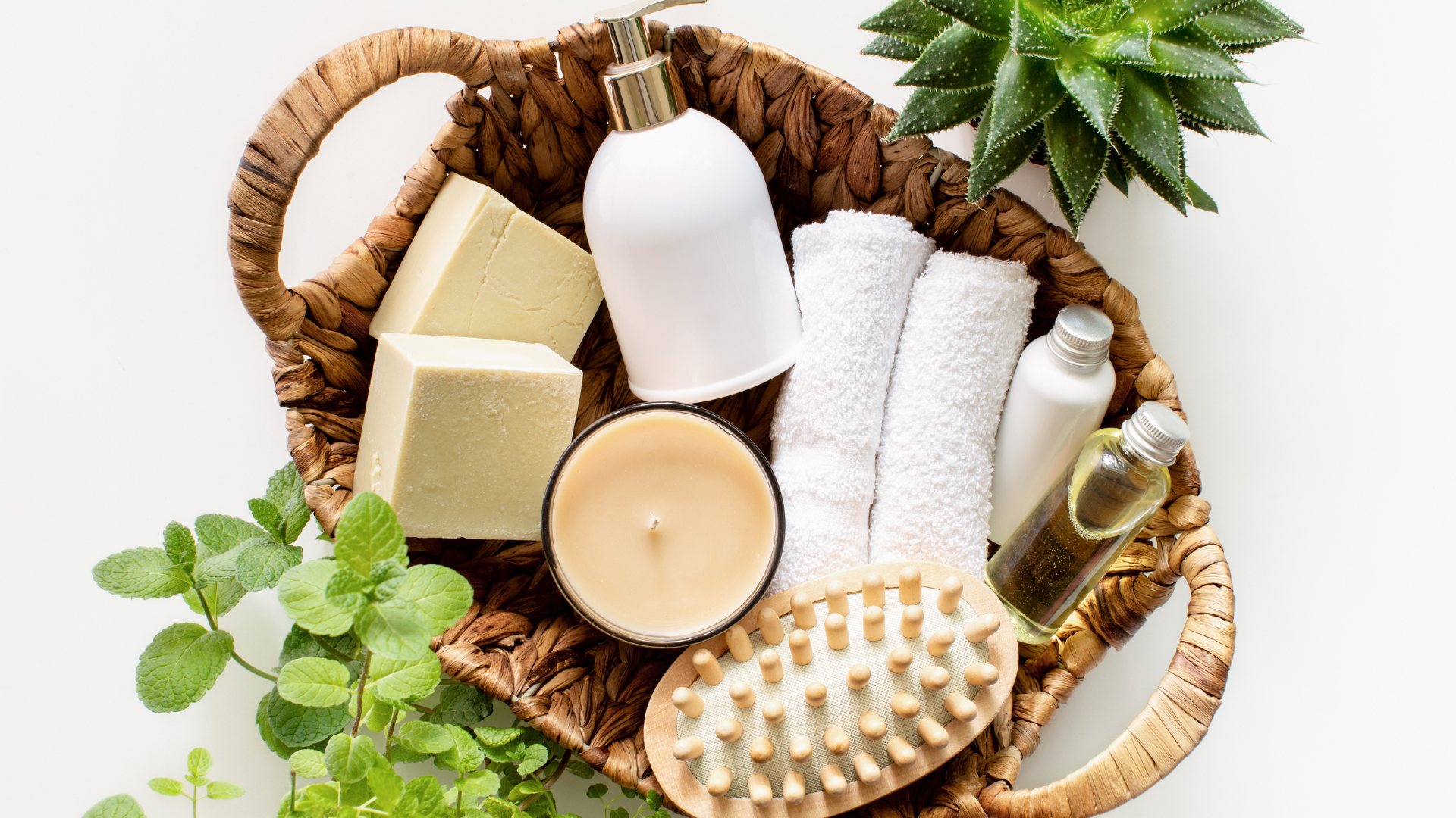 A wicker basket filled with soap , towels , brushes , candles and bottles.