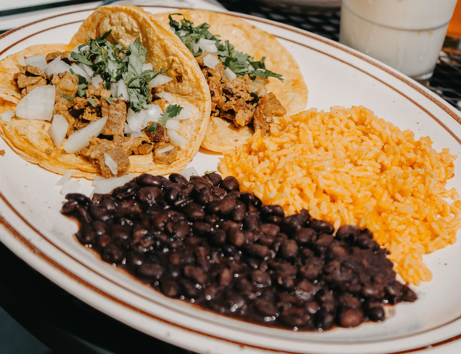 Tacos with rice and beans on a plate; corn tortillas filled with meat, onions, and cilantro.