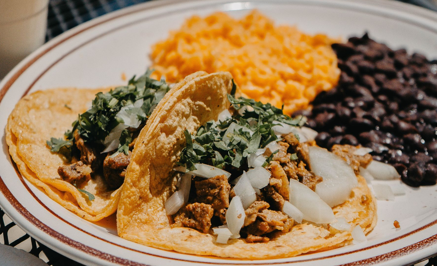 Tacos on a plate with rice and beans, garnished with cilantro and onions.