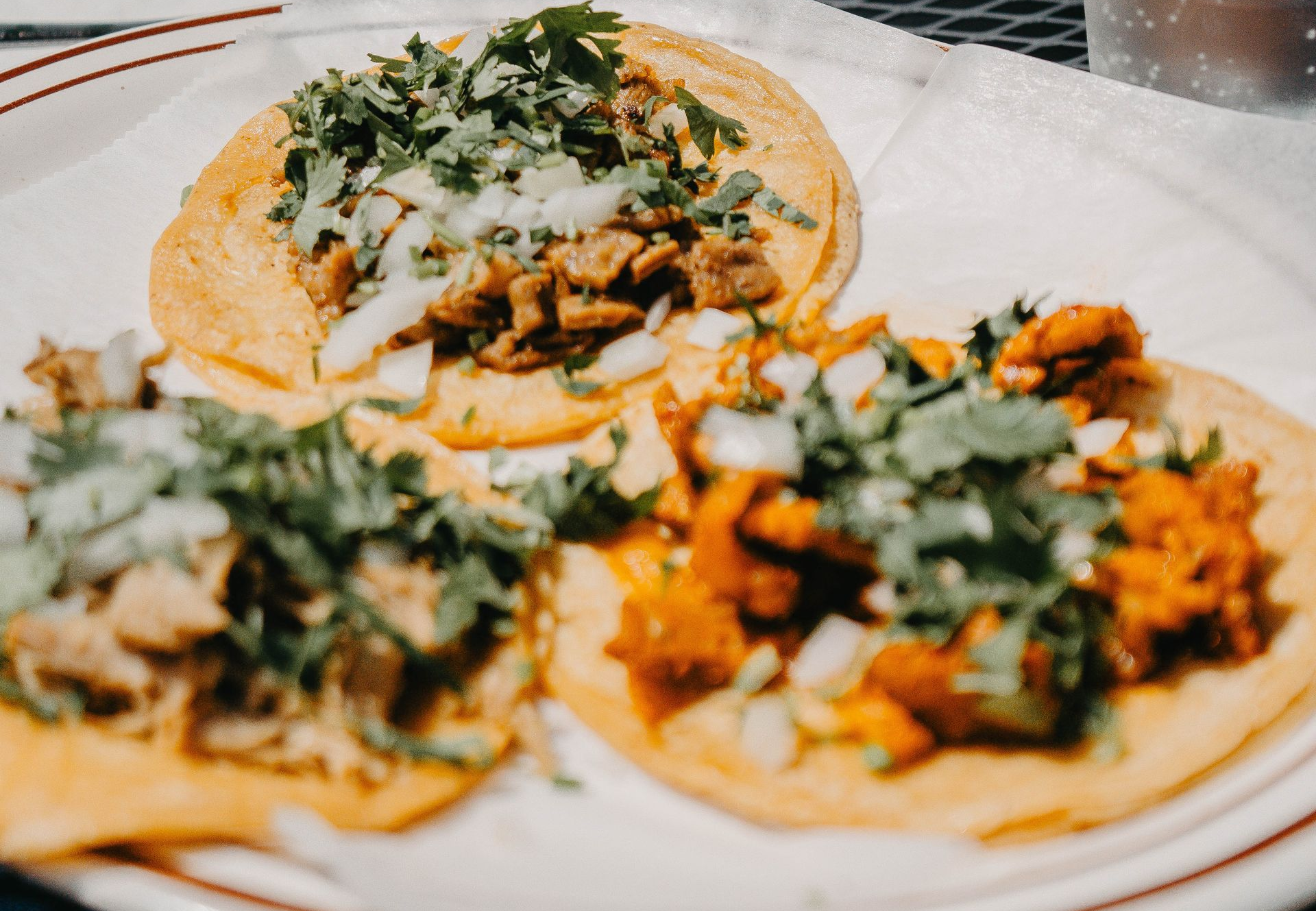 Three tacos with meat, cilantro, and onions on a white plate.
