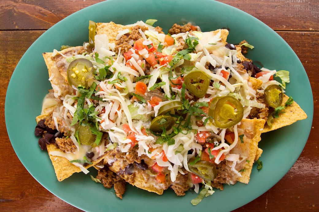Nachos on a green plate, topped with meat, cheese, jalapeños, and vegetables.