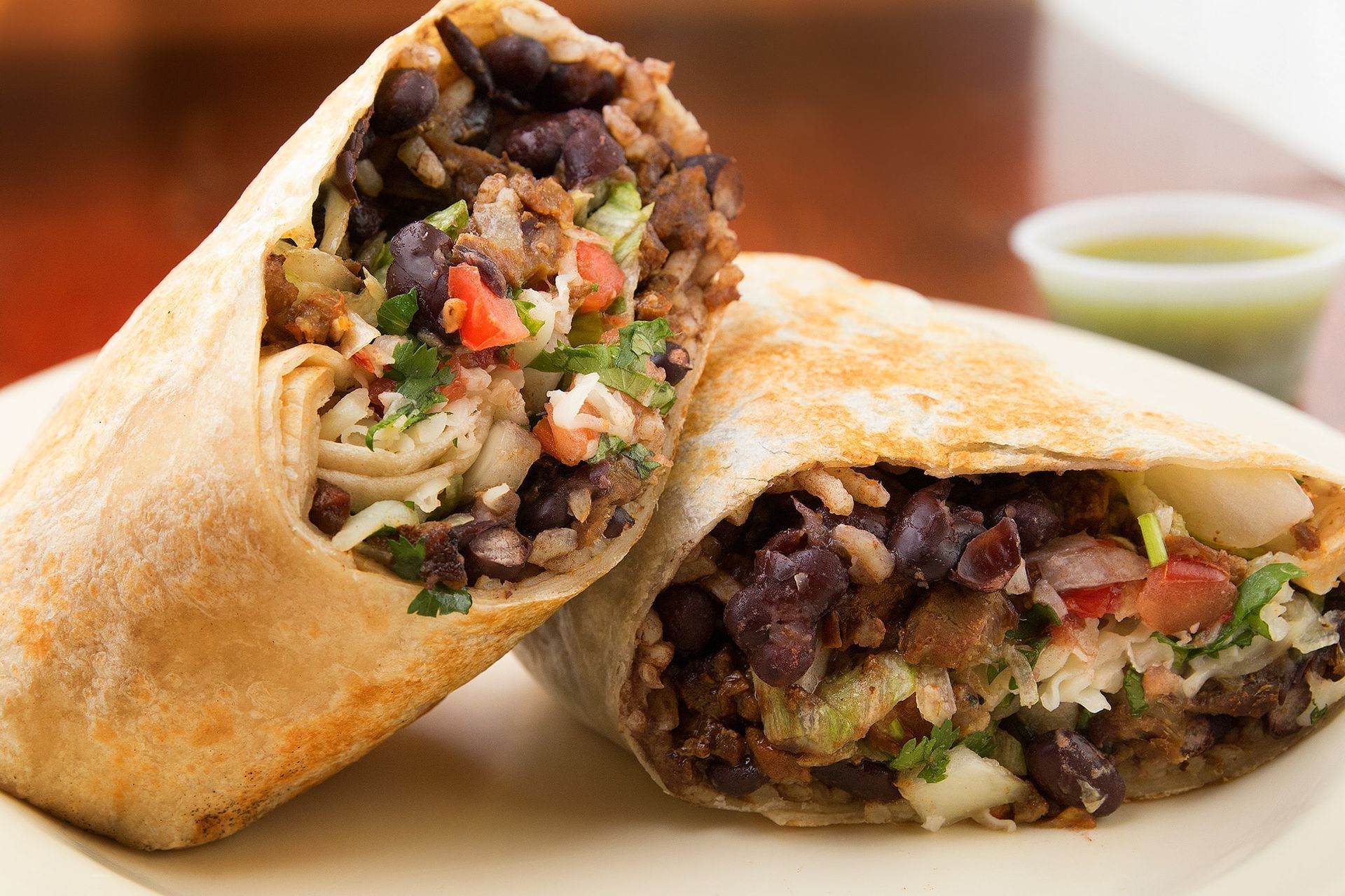 Burrito cut in half, filled with rice, black beans, and vegetables, on a plate.