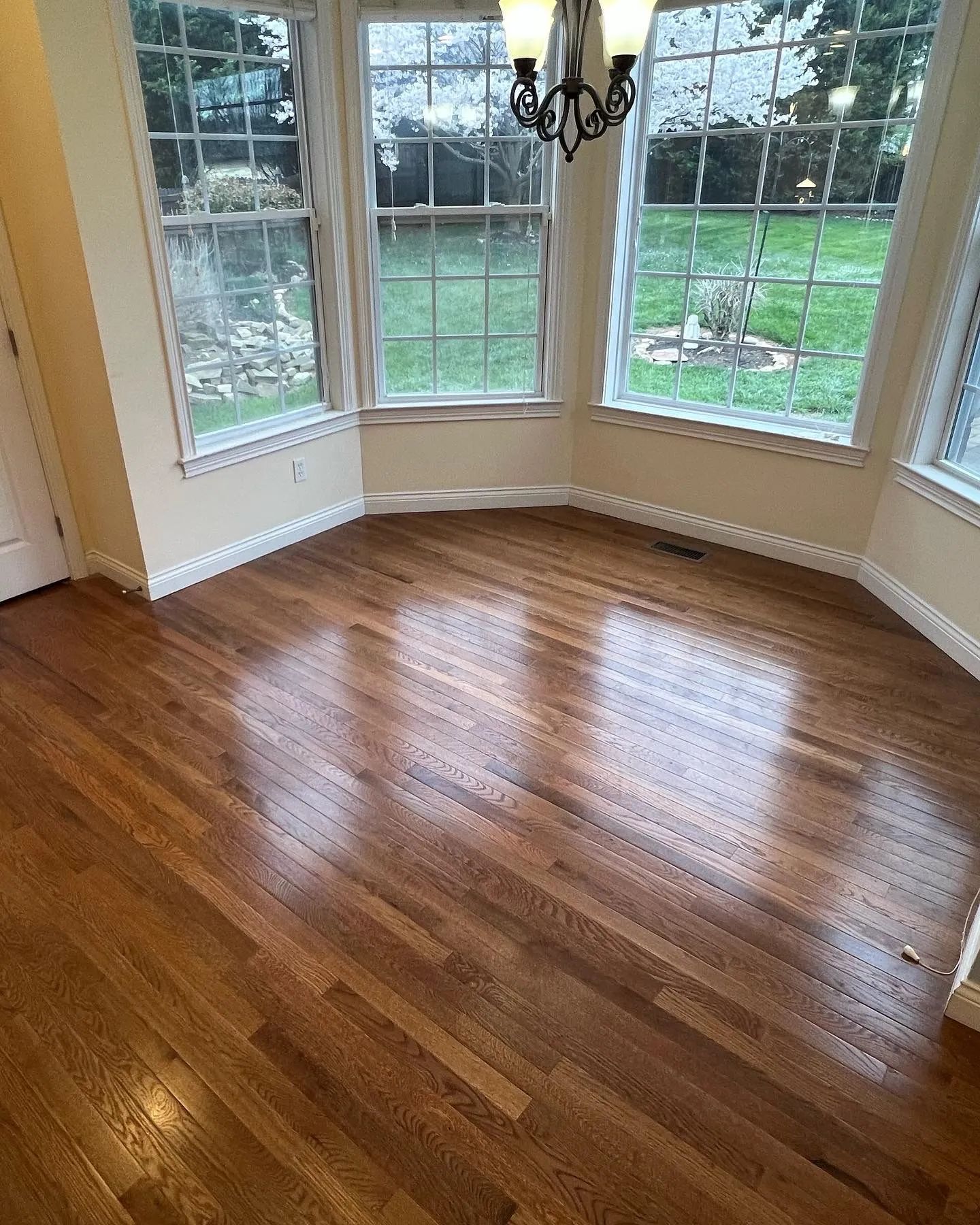 Hardwood floors in a room with three large windows and a chandelier.