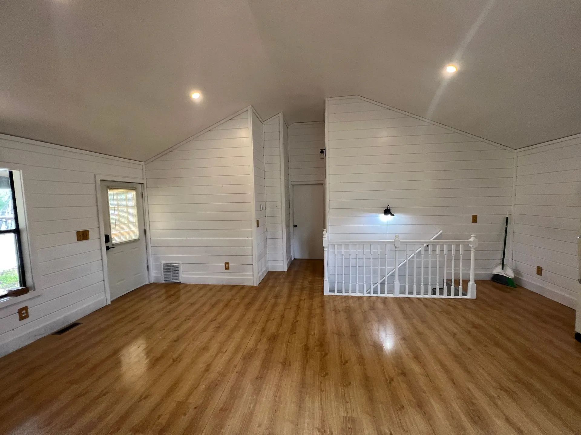 Empty room with wood floors, white plank walls, a door, and a staircase.