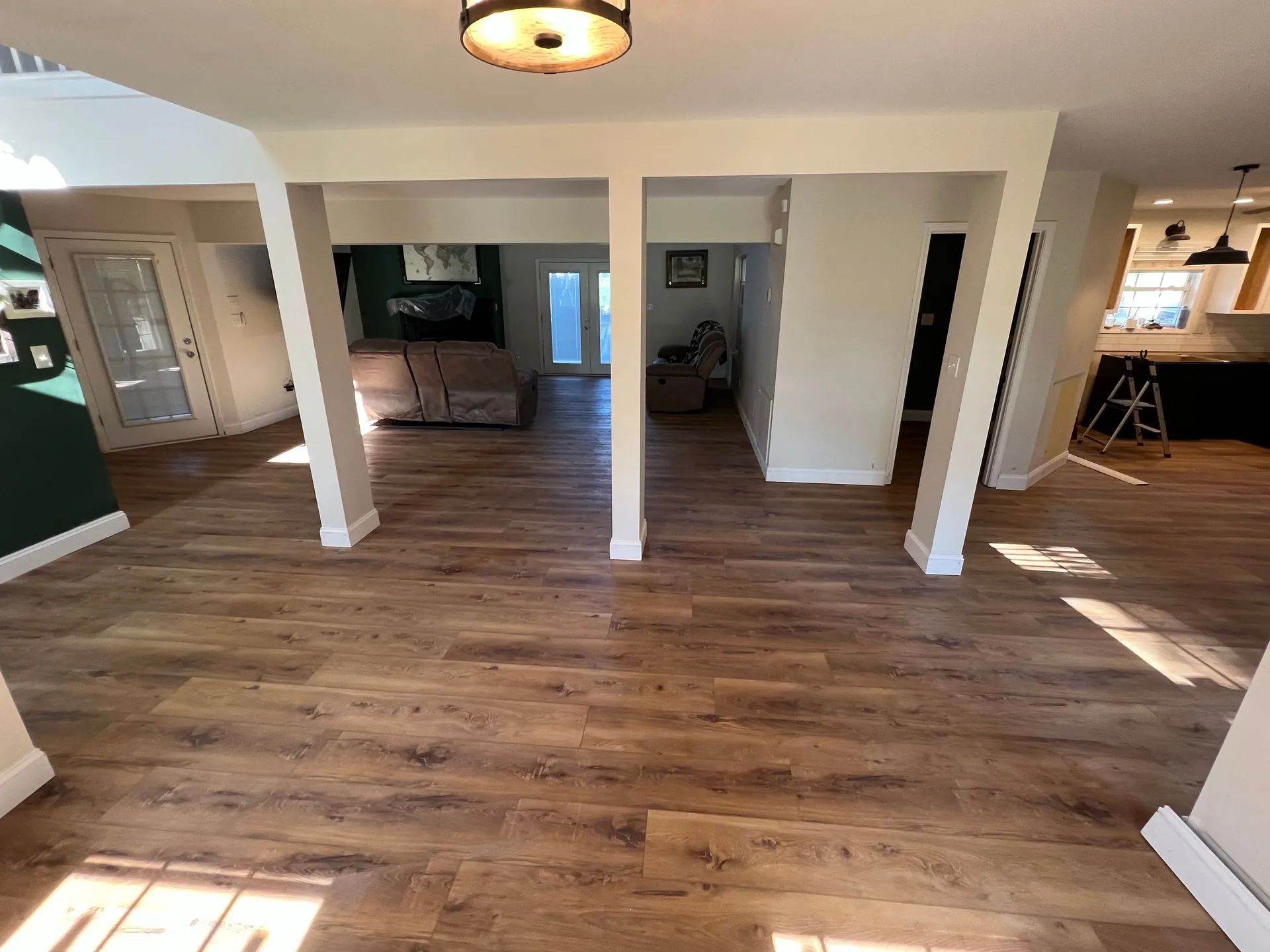 Open-plan living space with wood-look floors, white columns, and access to different rooms.