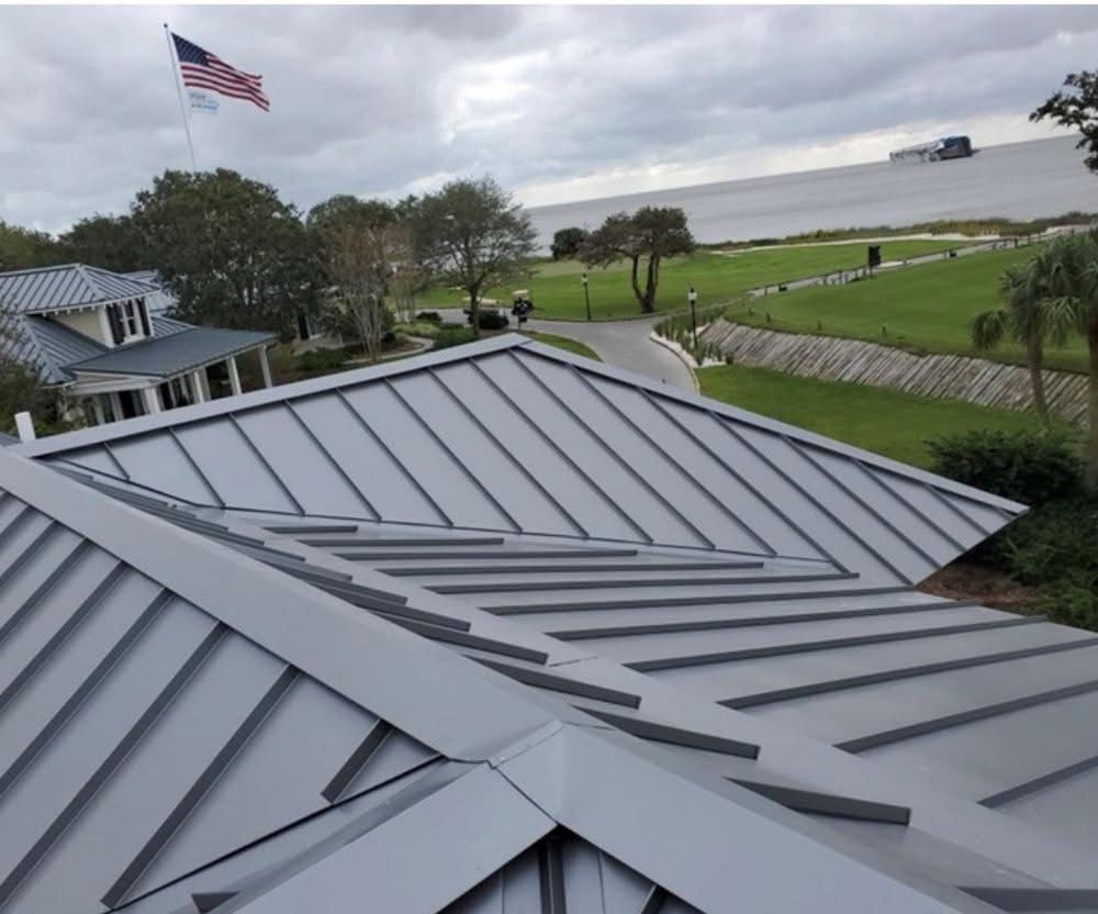 Gray metal roof of a building with American flag, overlooking a waterfront and a roadway.