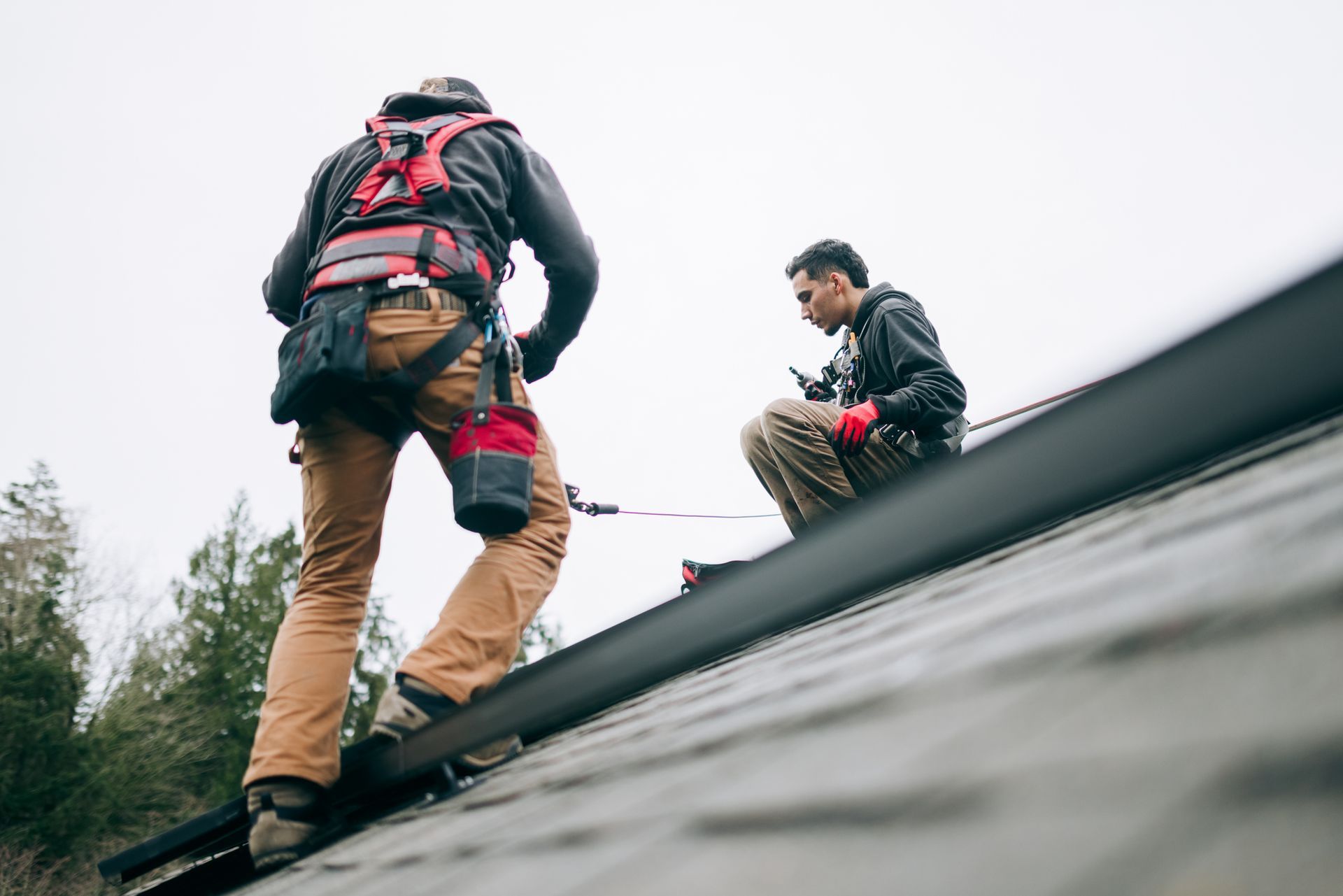 Roofing contractors using safety harnesses while working on a residential roof installation.
