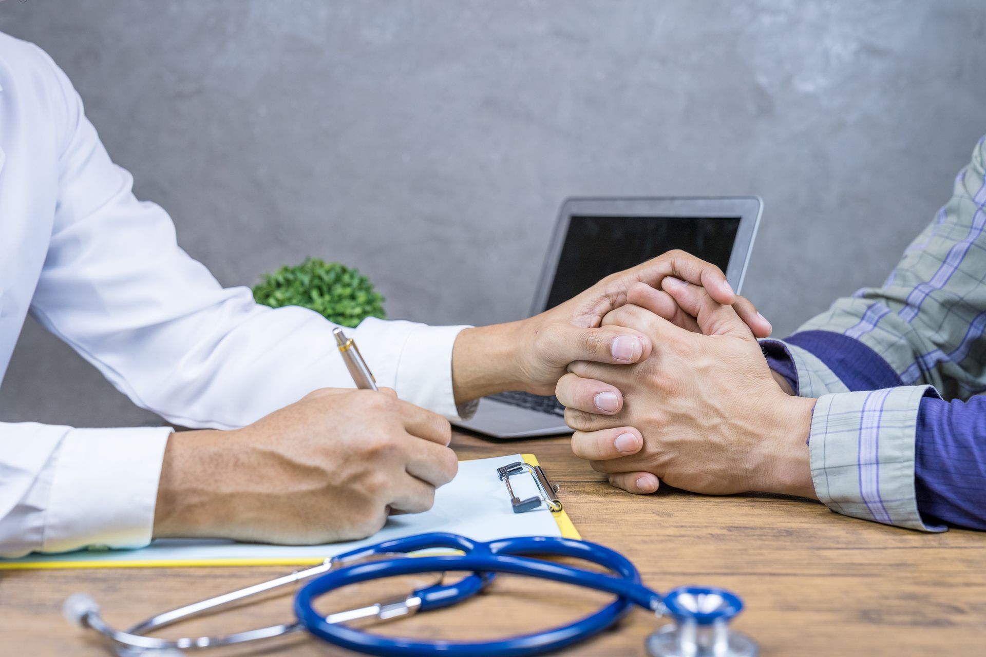 A doctor is holding a patient 's hand while writing on a clipboard.