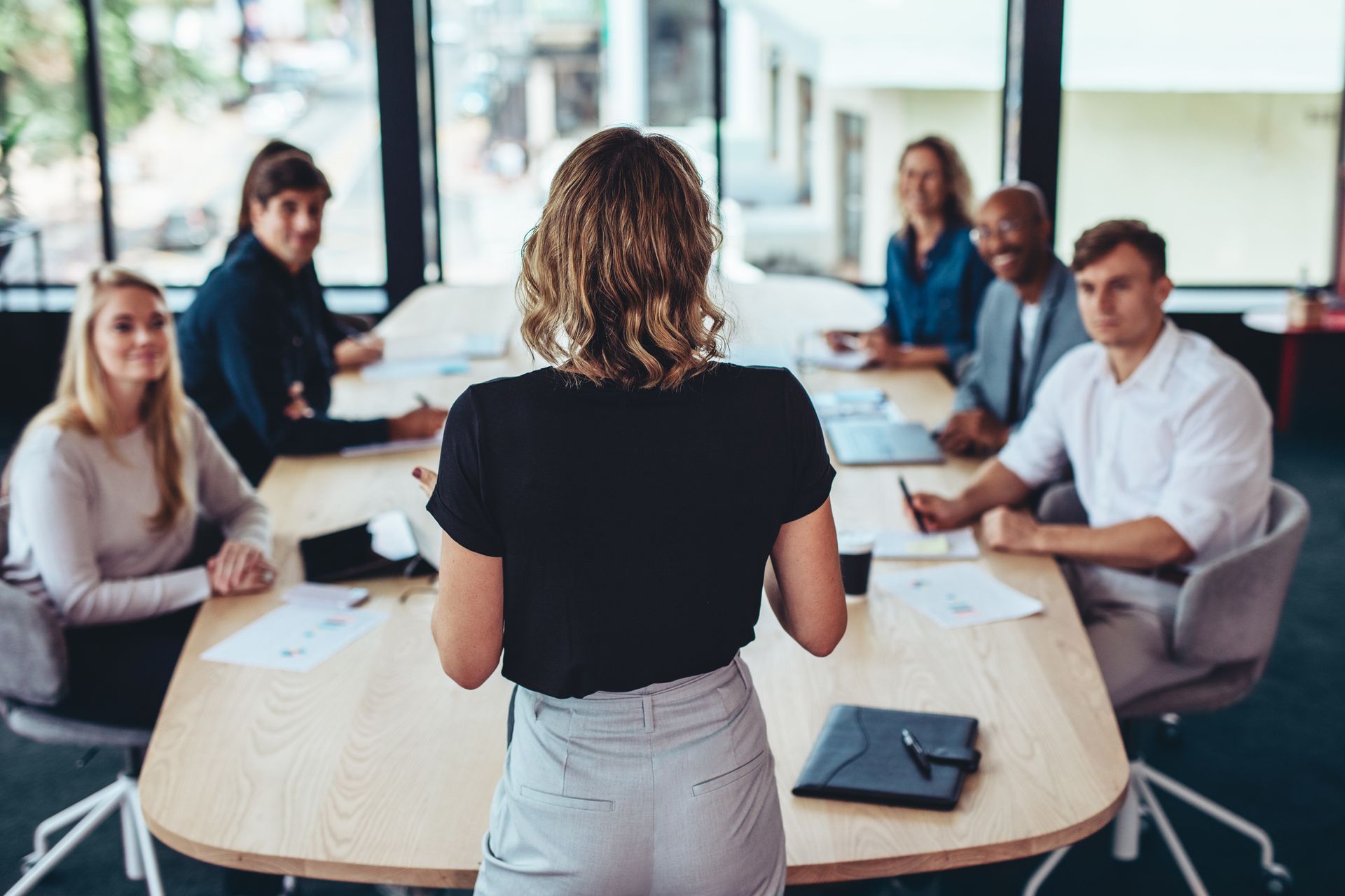A woman is giving a presentation to a group of people sitting around a table.