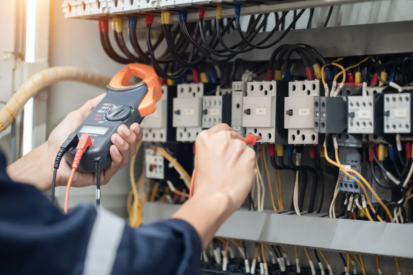Electrician using a multimeter to inspect electrical wiring in a control panel.