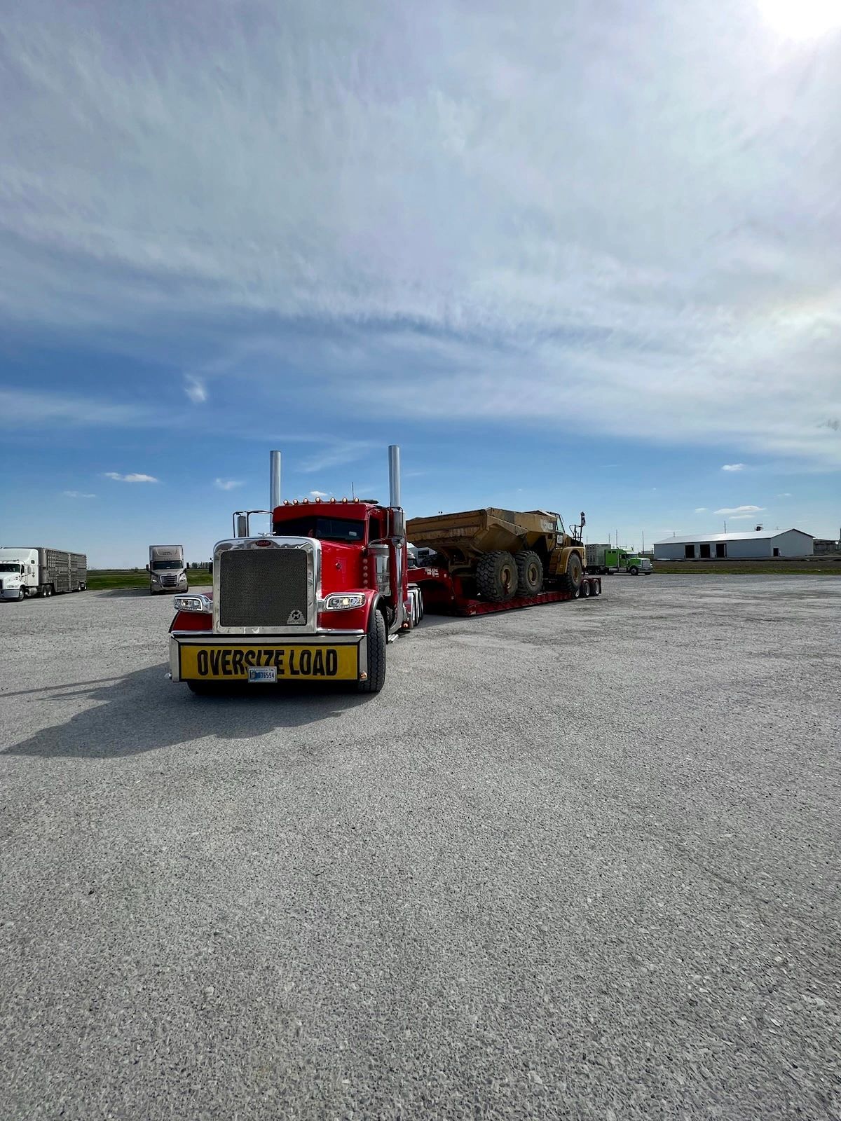 A red semi truck is parked in a gravel lot.