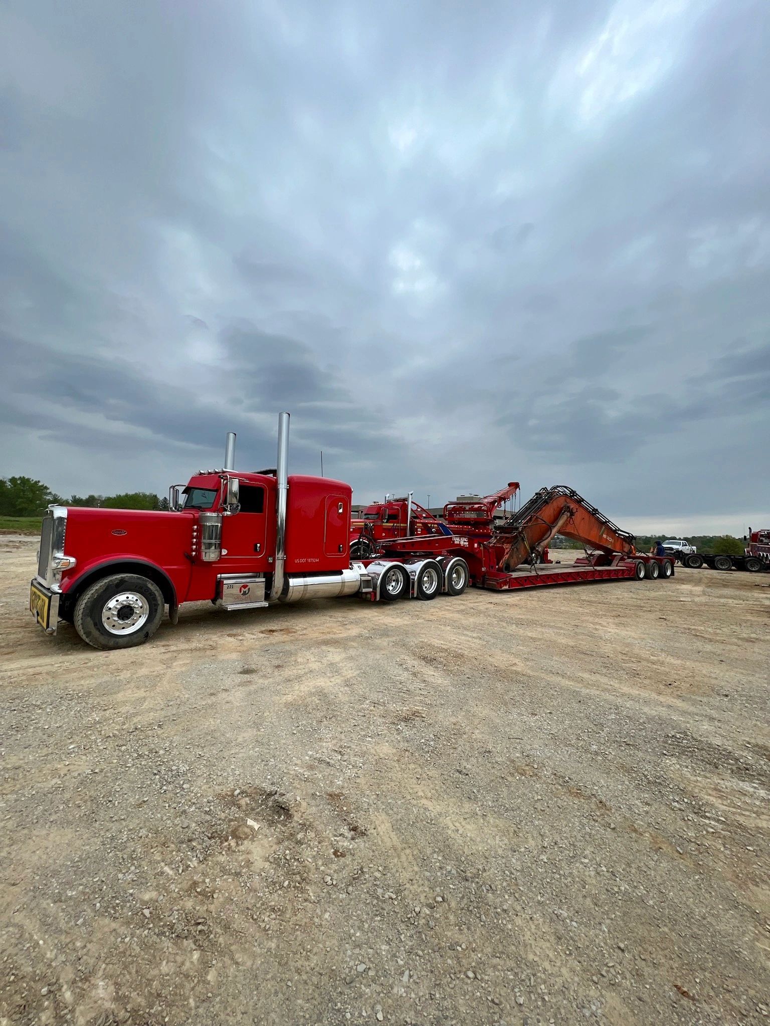 A red semi truck is parked in a dirt field.