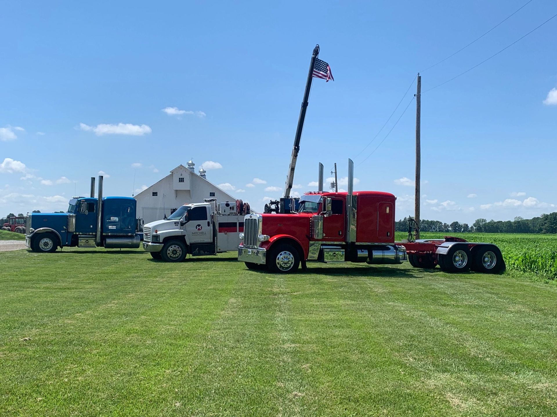 Three semi trucks are parked in a grassy field.