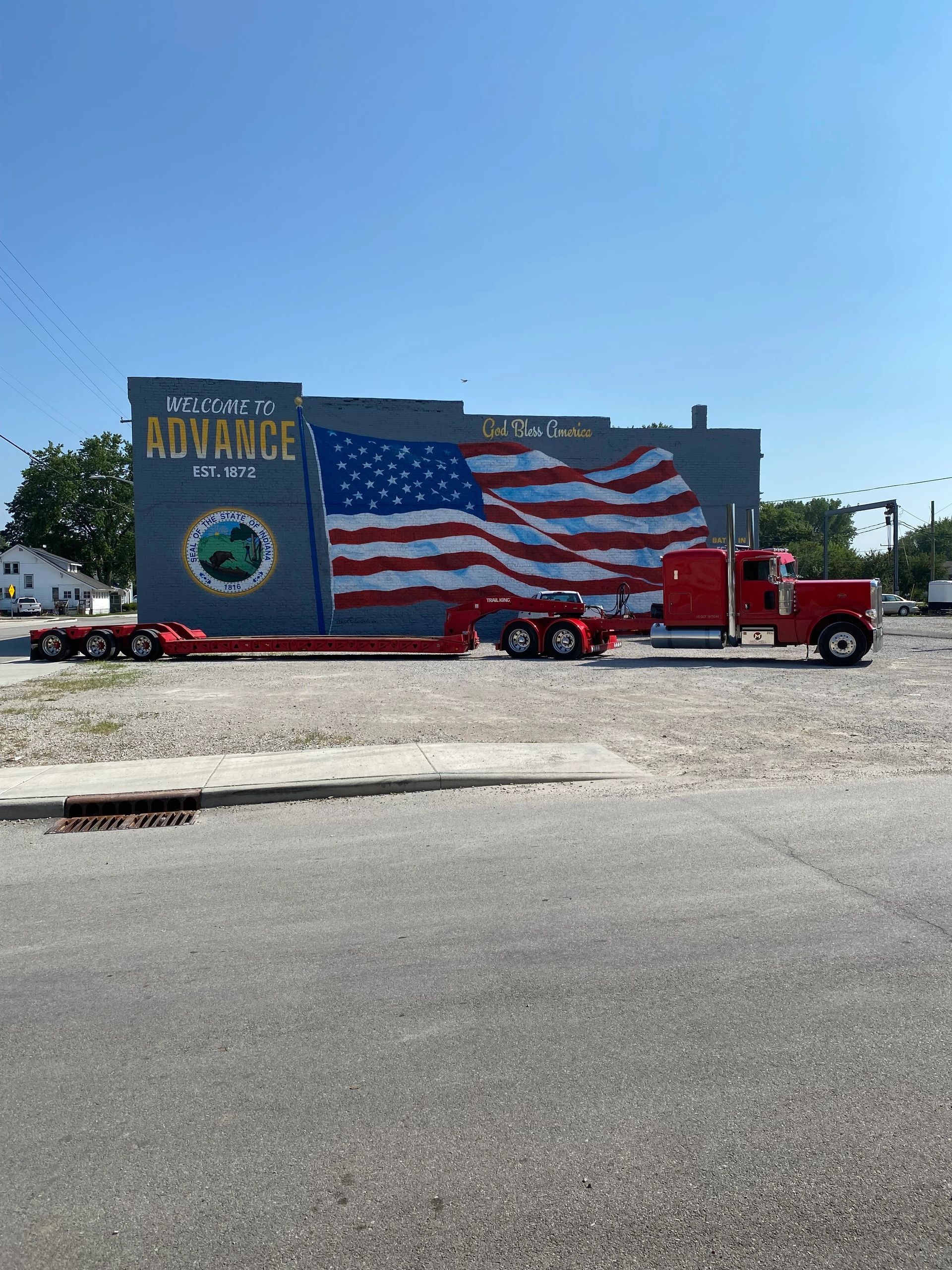 A red truck is parked in front of a building with an american flag painted on it.