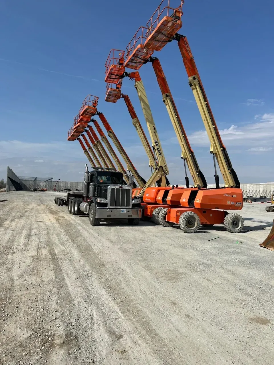 A row of construction vehicles are parked in a dirt lot