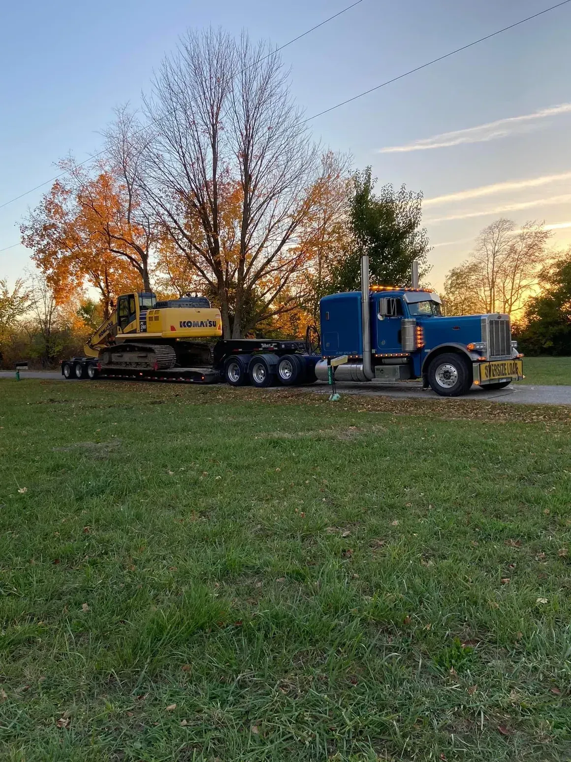 A blue semi truck is carrying a yellow excavator on a trailer.