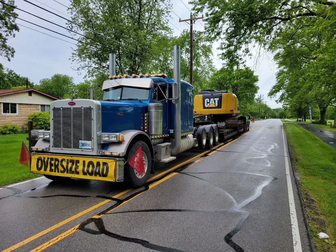 A blue semi truck is carrying an excavator down a road.