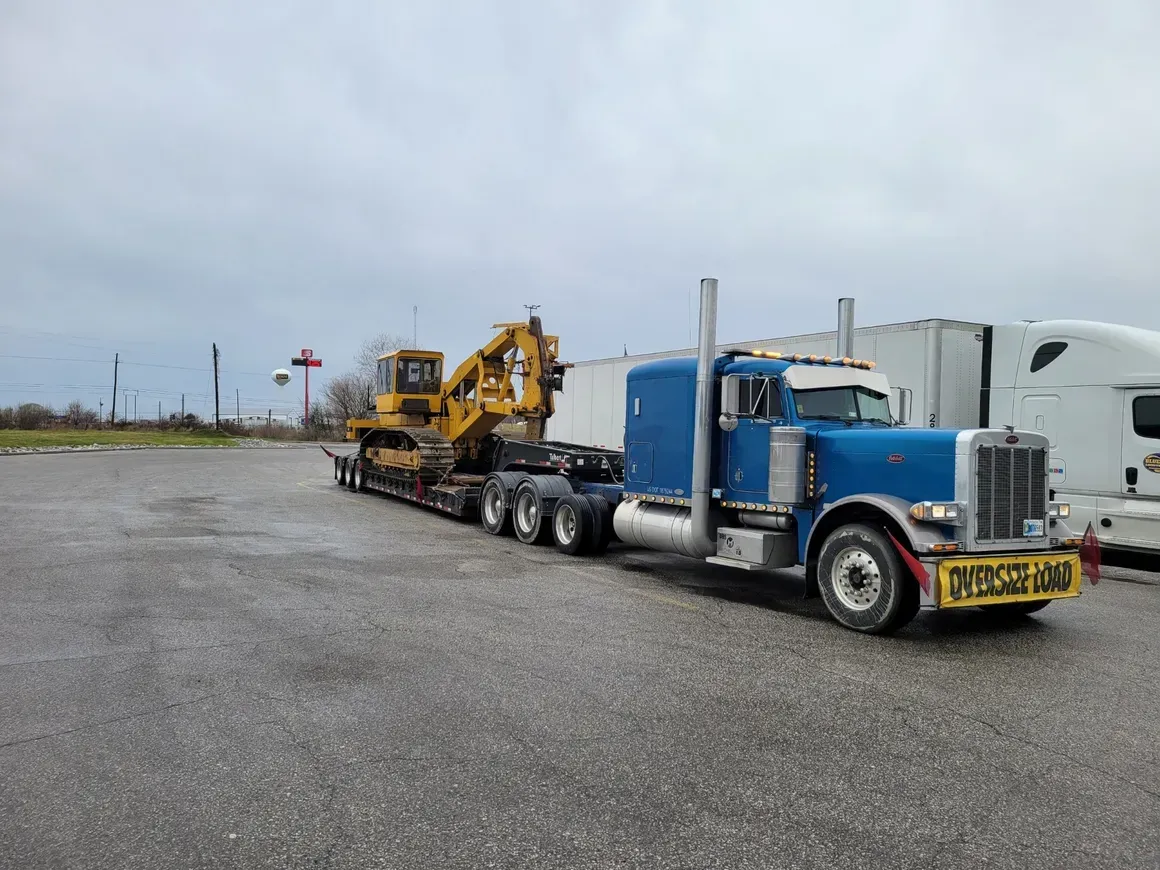 A blue semi truck is carrying a bulldozer on a trailer.