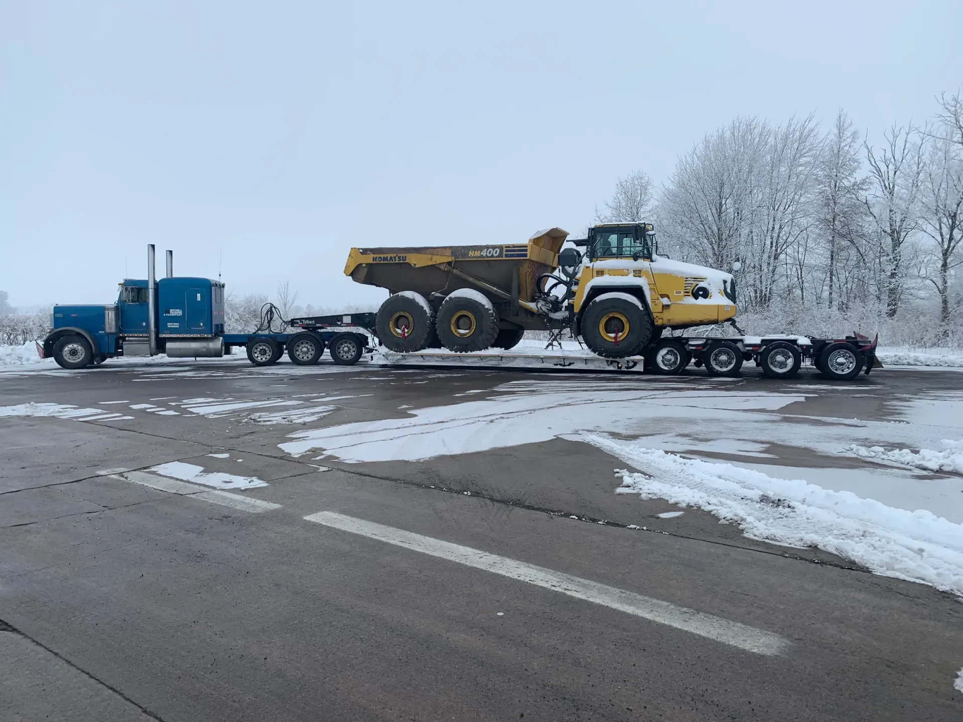 A dump truck is being towed by a semi truck on a snowy road.