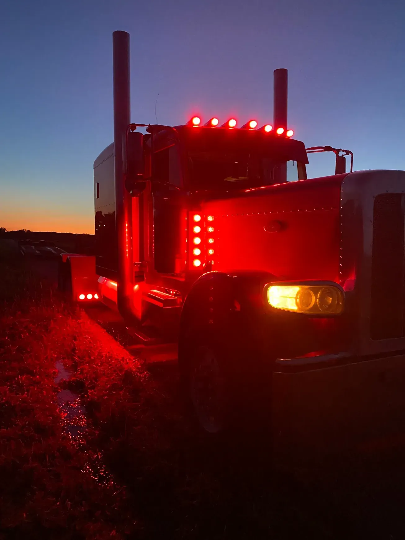 A semi truck with red lights on the front is parked in a field at night.