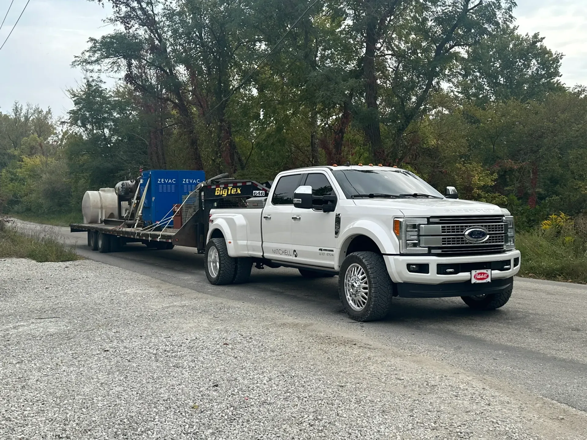 A white truck is towing a trailer down a gravel road.