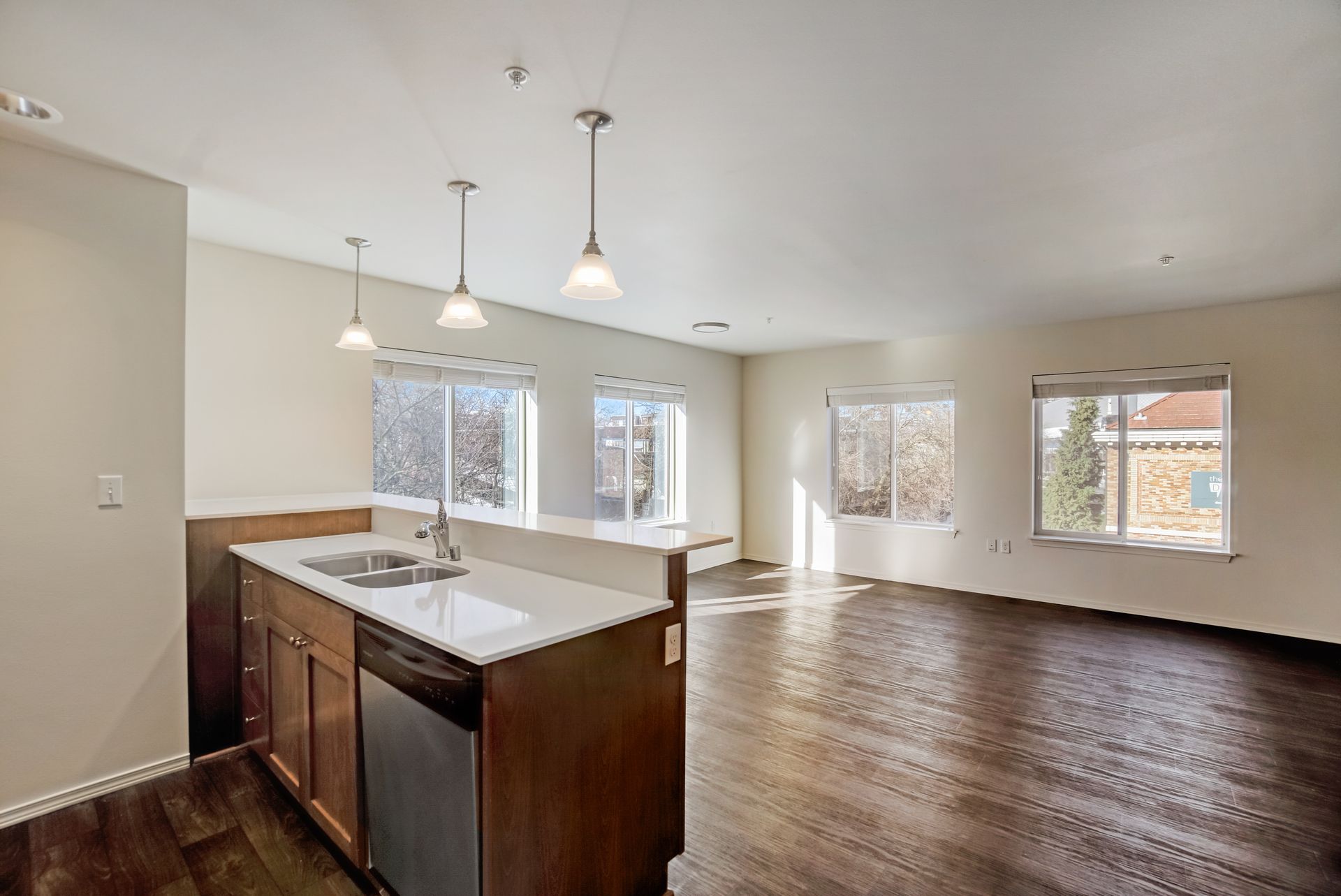 An empty kitchen with a sink , dishwasher , and hardwood floors.
