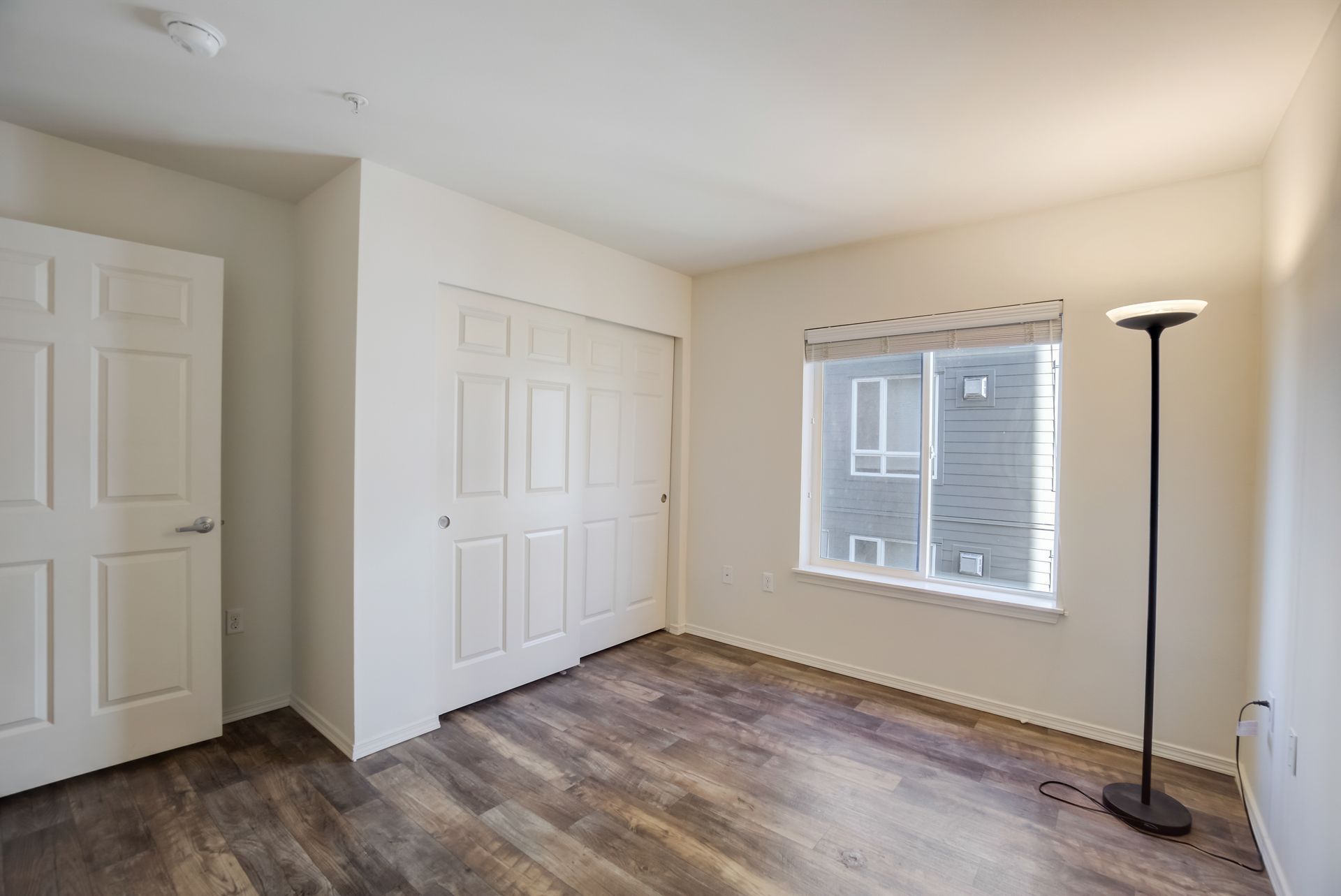 An empty bedroom with hardwood floors , a lamp and a window.