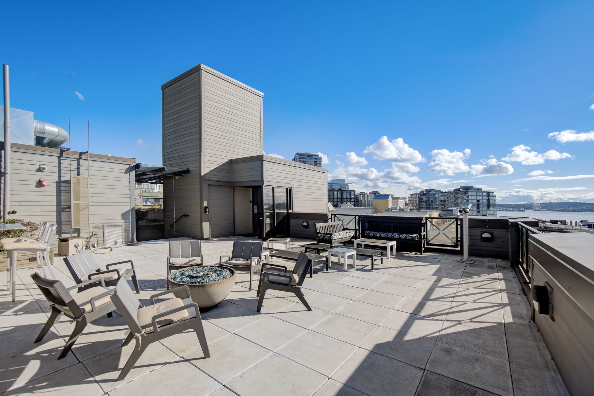 A rooftop patio with chairs , tables and a fire pit.