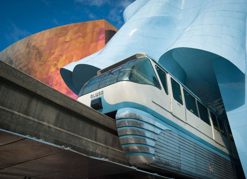 A train is going under a bridge in front of a building.