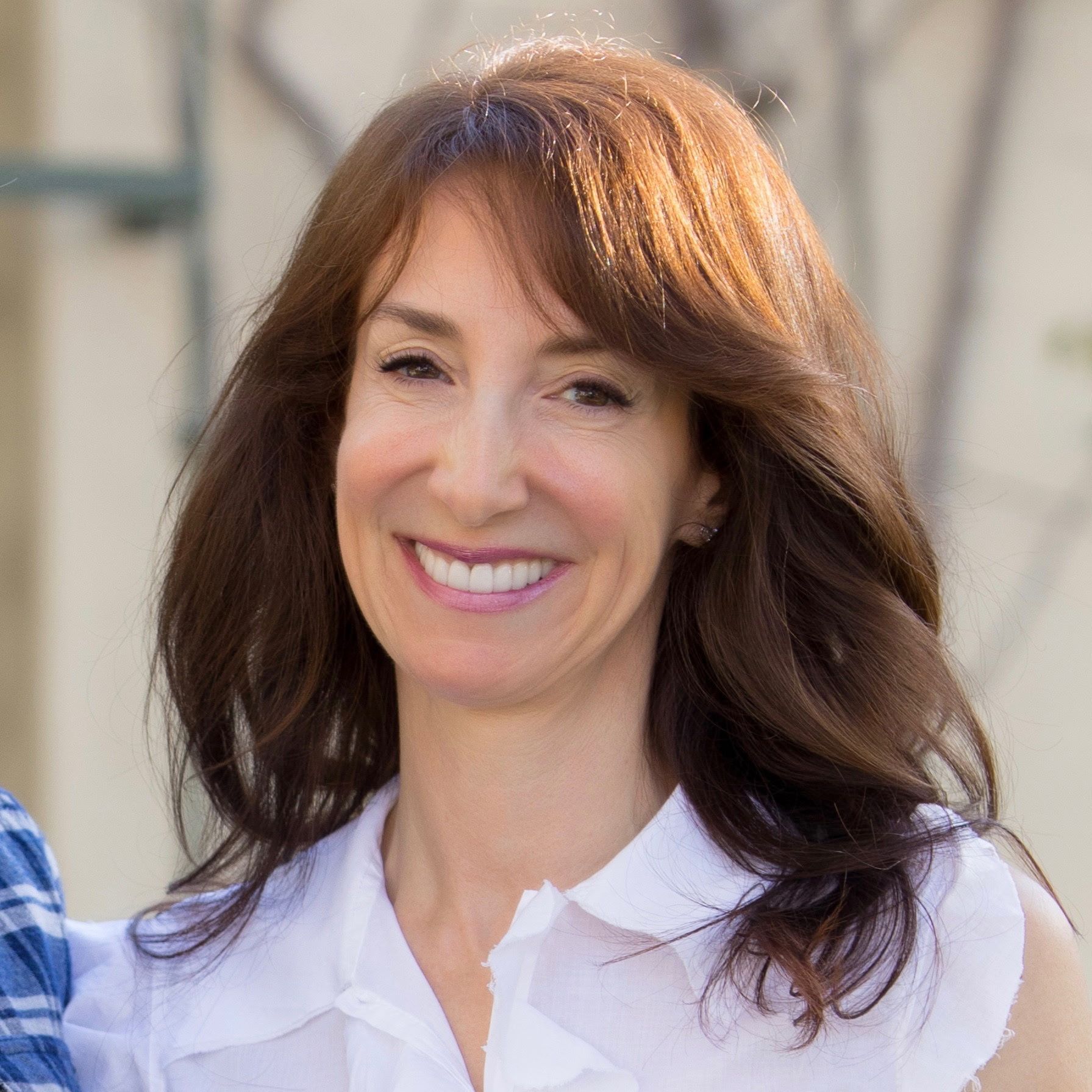 A woman with long brown hair is smiling and wearing a white shirt.
