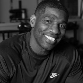 A black and white photo of a smiling man wearing a nike shirt