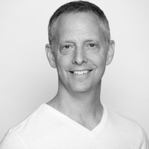 A man in a white shirt is smiling in a black and white photo.