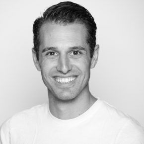 A man in a white shirt is smiling in a black and white photo.