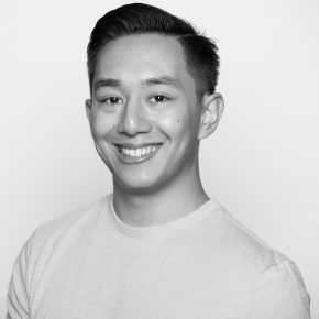 A man in a white shirt is smiling in a black and white photo.