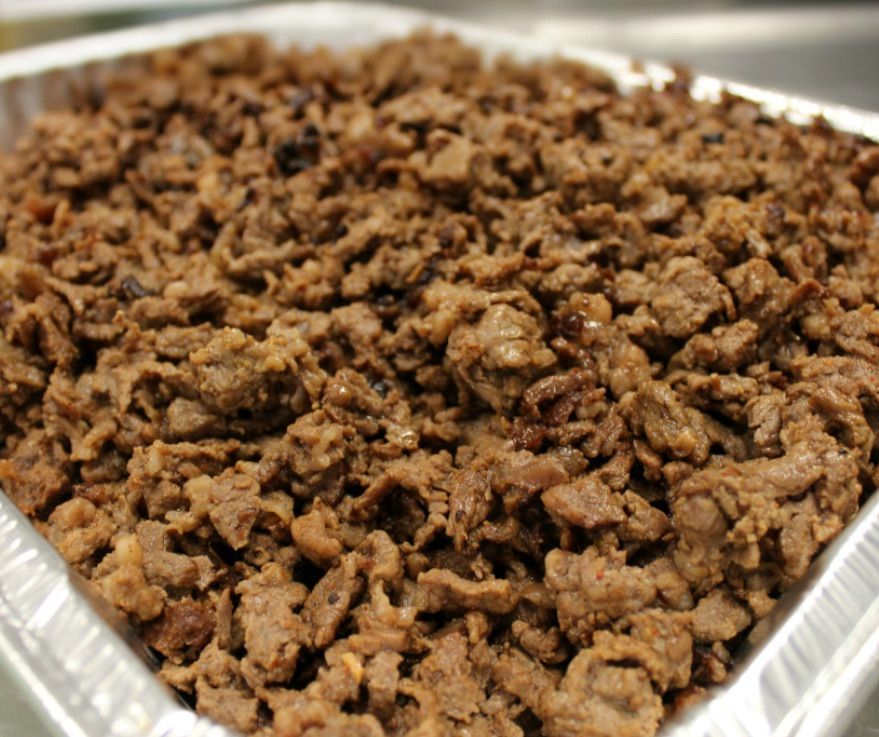 Three tacos topped with fresh pico de gallo and cilantro, served on a white plate on a patterned table.