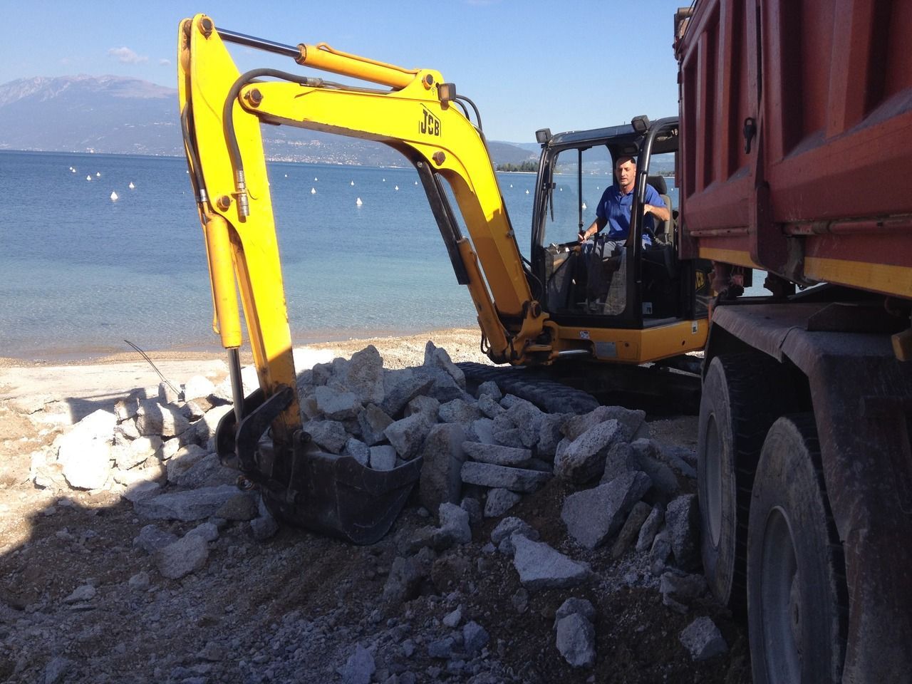 un uomo guida un escavatore giallo vicino sulla riva del lago